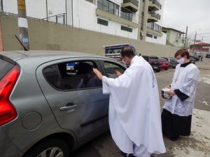 Padre Tiago Síbula abençoando um carro e seus passageiros durante o Drive Thru Solidário