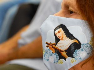Paroquiana com a máscara facial de Santa Rita  assistindo a missa da festa de Santa Rita de Cássia 2021